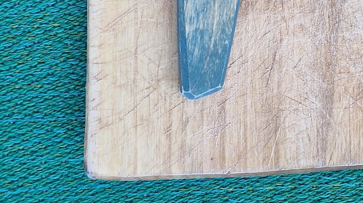 En detalj av ett bemålat skaft av ett täljt träföremål med patina.